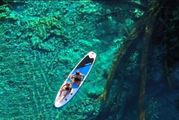 Vista aérea con dron de una canoa tradicional navegando sobre las aguas cristalinas del lago Paisu Pok en la isla de Peleng.