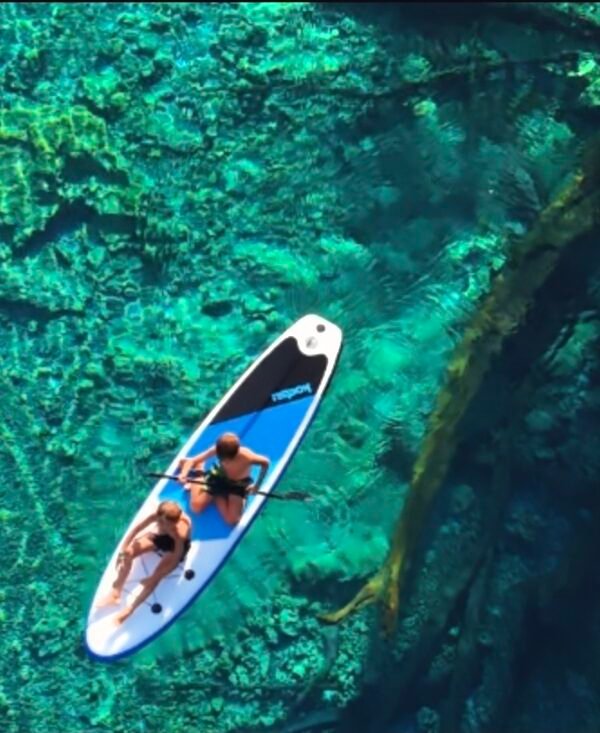 Vista aérea con dron de una canoa tradicional navegando sobre las aguas cristalinas del lago Paisu Pok en la isla de Peleng.