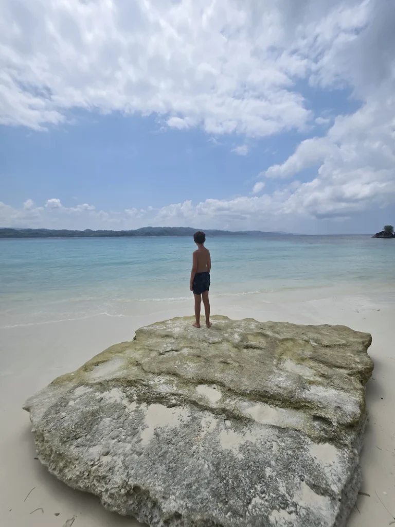 Viajero sobre una roca en las tranquilas aguas turquesas de Pantai Oyama en Banggai Laut durante una expedición costera privada de turismo lento.