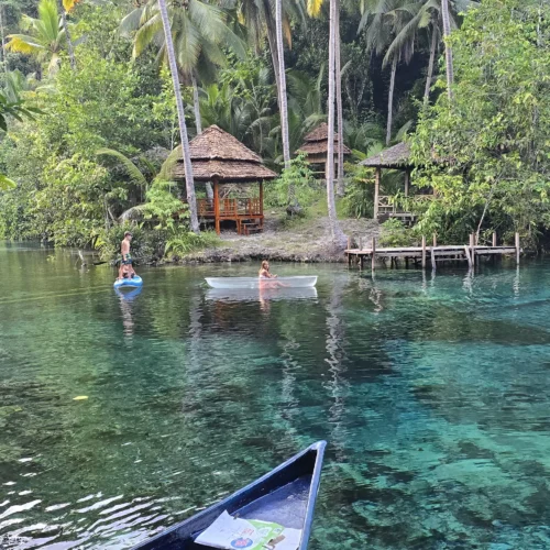 Lago azul cristalino de Paisupok en las Islas Banggai, Indonesia, con barcas y cabañas rodeadas de selva tropical.