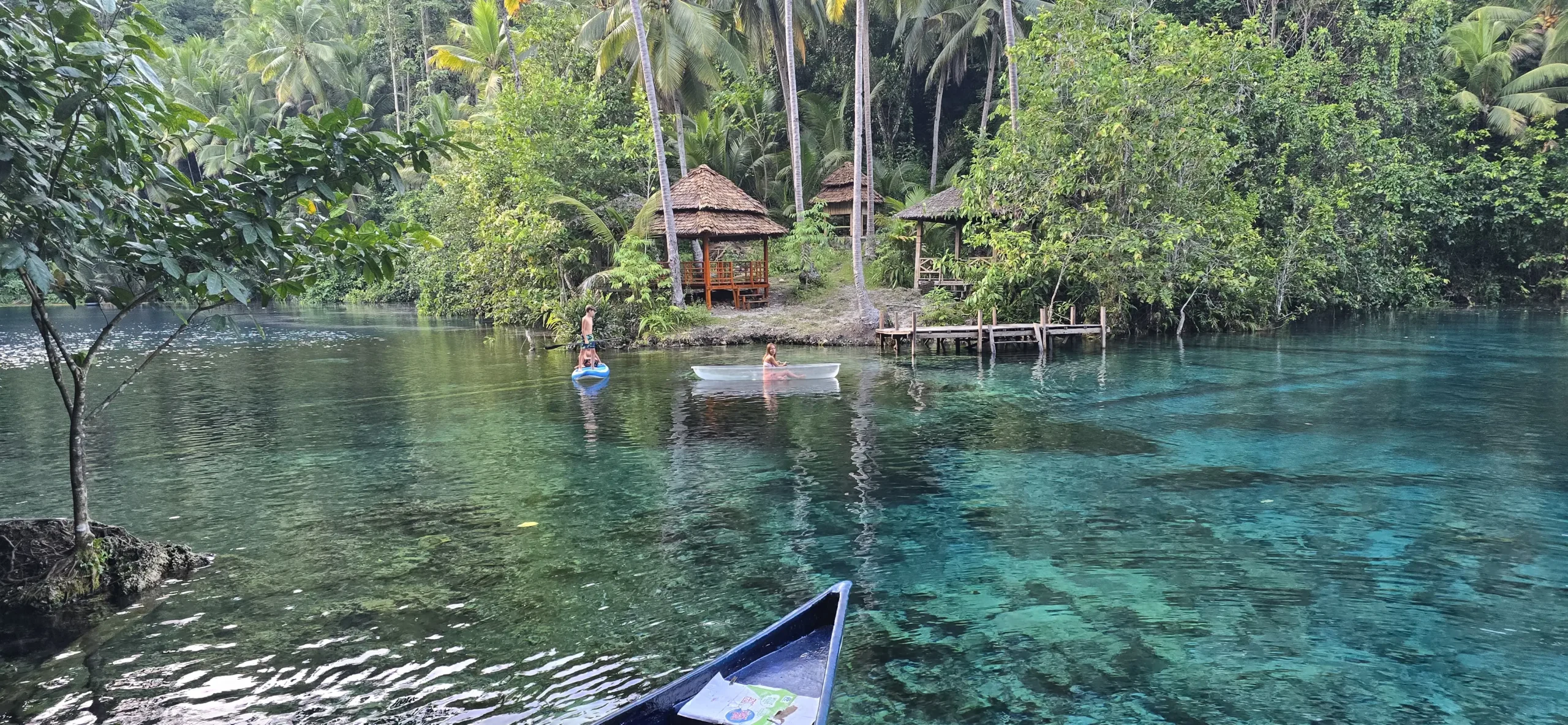 Lago azul cristalino de Paisupok en las Islas Banggai, Indonesia, con barcas y cabañas rodeadas de selva tropical.