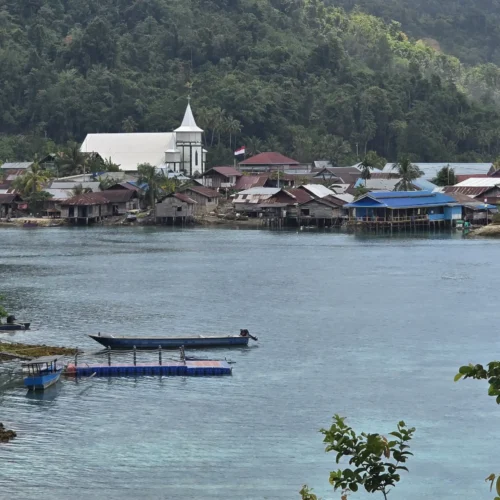 Vista del pueblo costero de Paisupok en las Islas Banggai, destacando su característica iglesia cristiana blanca frente al mar y rodeada de densa vegetación tropical.