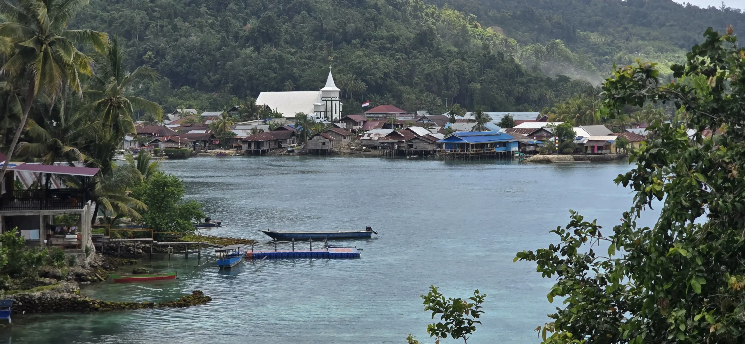 Vista del pueblo costero de Paisupok en las Islas Banggai, destacando su característica iglesia cristiana blanca frente al mar y rodeada de densa vegetación tropical.