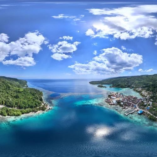 Vista panorámica aérea del pueblo de Paisupok y la Bahía Kawalu en las Islas Banggai, mostrando la costa, casas tradicionales, selva tropical y aguas turquesas.