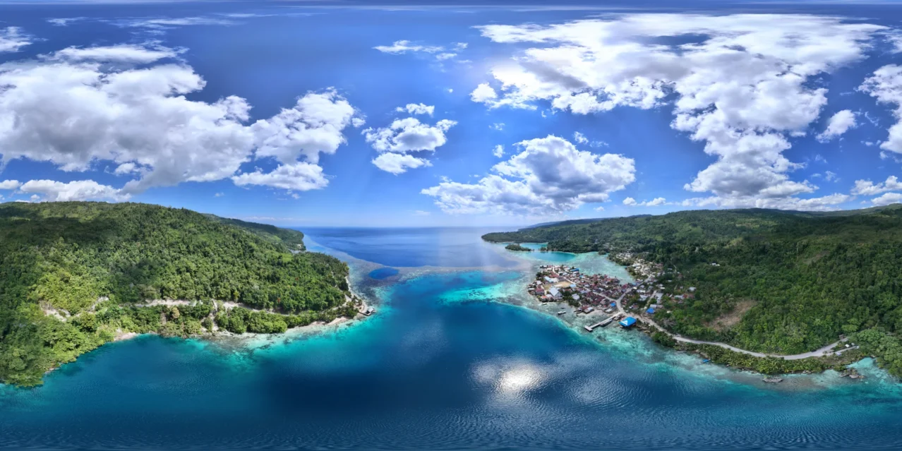 Vista panorámica aérea del pueblo de Paisupok y la Bahía Kawalu en las Islas Banggai, mostrando la costa, casas tradicionales, selva tropical y aguas turquesas.