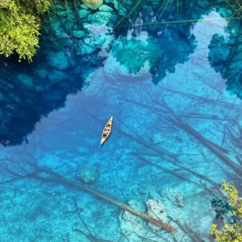 Vista aérea diurna del lago cristalino Paisu Pok rodeado de exuberante selva tropical en las islas Banggai, Indonesia. Una pequeña canoa navega sobre sus aguas transparentes.