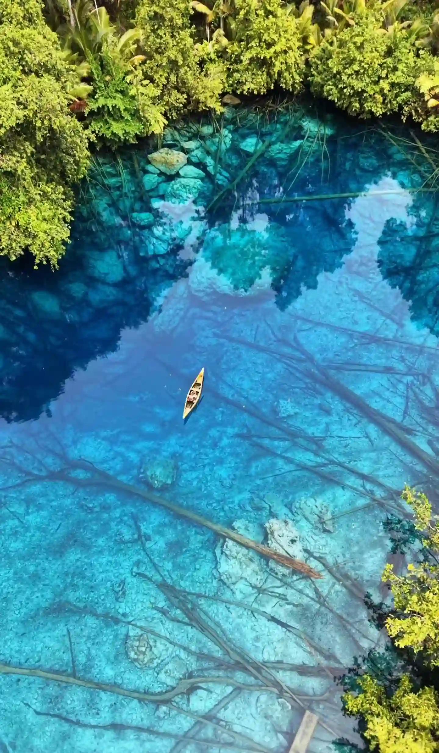 Vista aérea diurna del lago cristalino Paisu Pok rodeado de exuberante selva tropical en las islas Banggai, Indonesia. Una pequeña canoa navega sobre sus aguas transparentes.