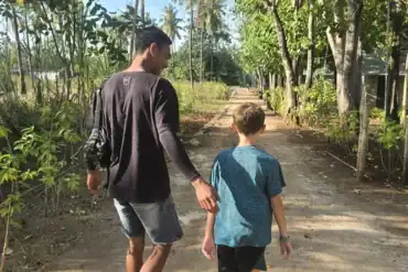 Guía local de Paisu Pok Tours caminando junto a un niño viajero durante una expedición privada para familias en la isla de Peleng.