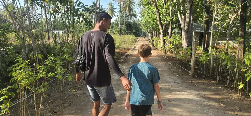 Guía local de Paisu Pok Tours caminando junto a un niño viajero durante una expedición privada para familias en la isla de Peleng.