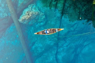 Vista aérea de una pequeña canoa navegando sobre las aguas turquesas y cristalinas del lago kárstico Paisu Pok en las islas Banggai, Indonesia.