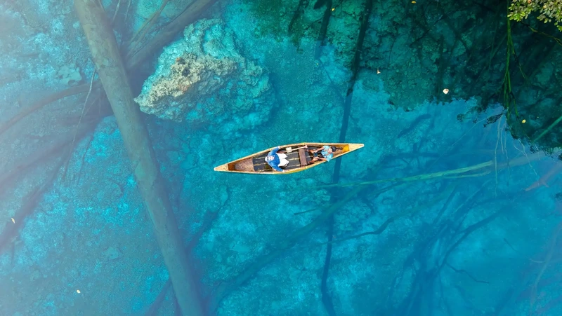 Vista aérea de una pequeña canoa navegando sobre las aguas turquesas y cristalinas del lago kárstico Paisu Pok en las islas Banggai, Indonesia.