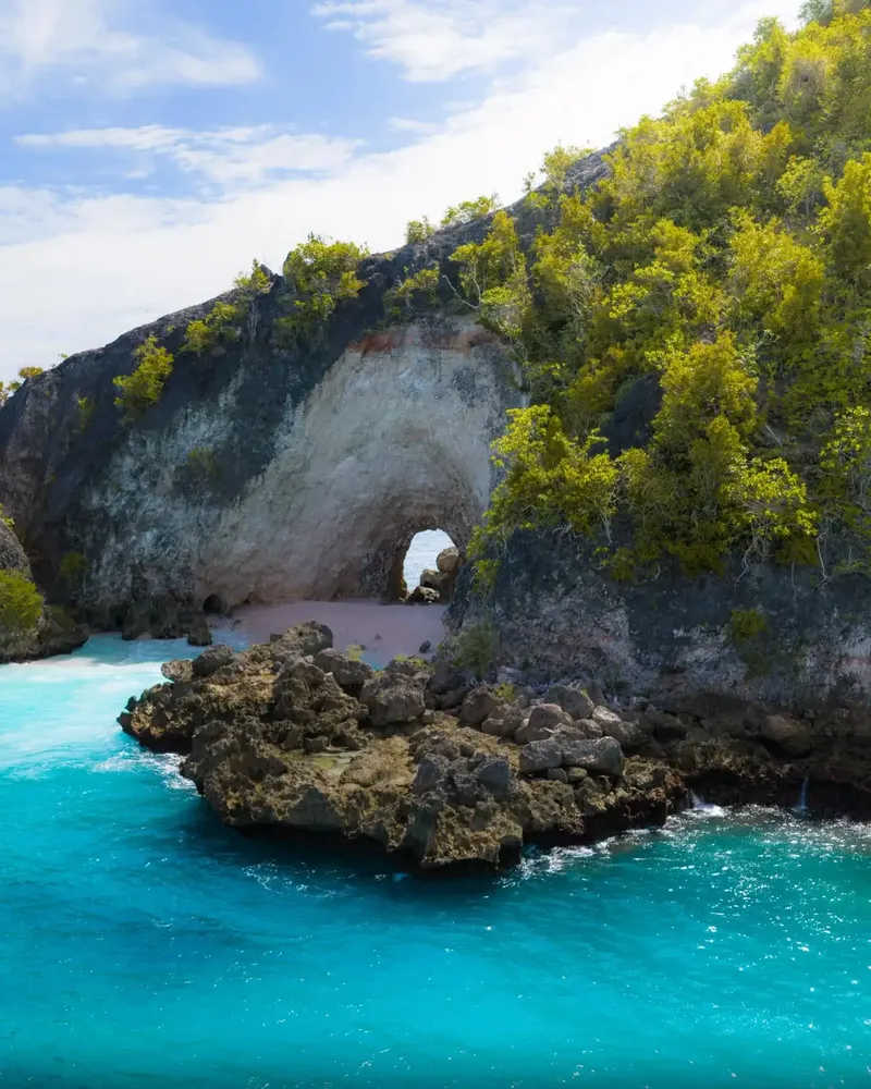 El majestuoso arco de roca caliza natural de Tanjung Gundul o Batu Tumpeng en Banggai Laut sobre aguas cristalinas turquesas, explorado en nuestra expedición marina privada.