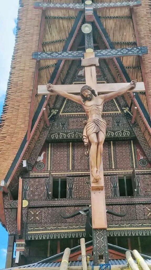 Cruz cristiana frente a la fachada de una casa tradicional Tongkonan en Toraja
