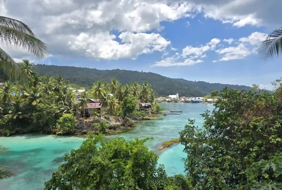 Panorámica de bahía de aguas turquesas rodeada de palmeras y aldea costera en las islas de Peleng y Banggai